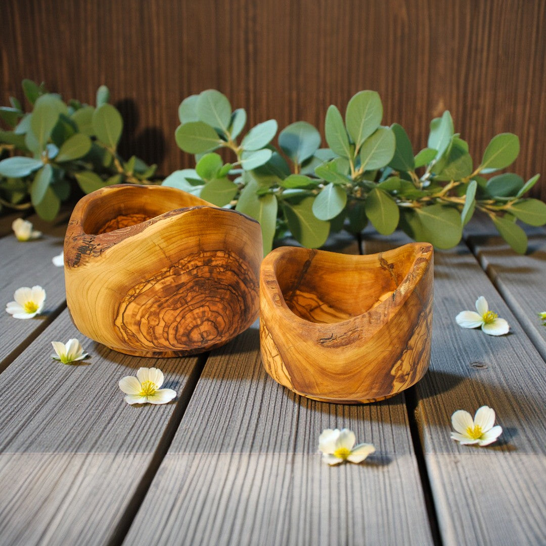 Twee handgemaakte olijfhouten kommen op een houten ondergrond, omringd door witte bloemen en groene takjes
